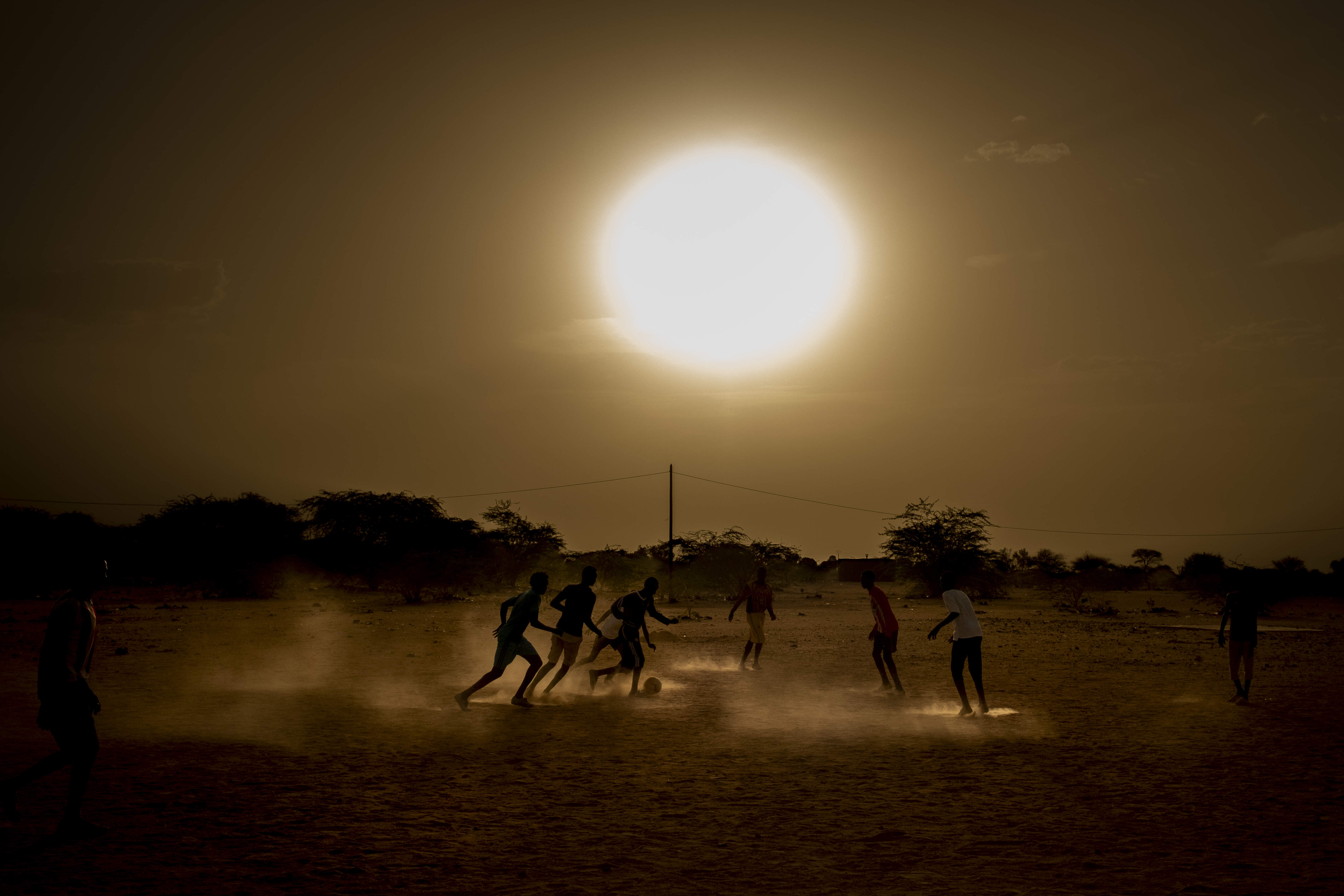 Sudanese migrants, children and men together, play football outside a 'hostel', provided by the United Nations, for migrants who are being forcibly sent home from Algeria and Libya in Agadez, Niger, on May 11, 2018. In May 2018, between the sun and the dusty wind, the temperatures in Agadez, Niger are about 45 degrees celsius. The region is known for uranium and salt mines, though it has become infamous as the last way station for migrants and refugees who are being smuggled to Europe, or Algeria and Libya