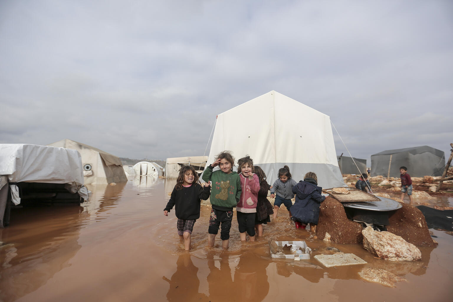 On 19 January 2021, children stand in a flooded area of Kafr Losin Camp in northwest Syrian Arab Republic. Over the past few days, western Aleppo and Idlib governorates in the northwest of the country have been experiencing some of the heaviest winter storms so far this season. The heavy rainfall has flooded tents and cut off roads leading to camps for internally displaced families. While the damage continues to be assessed, there are reports of more than 1,700 households in the area have been affected.