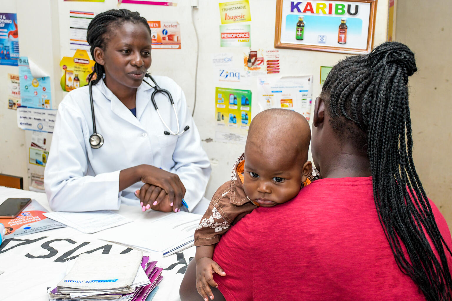 On 24 November 2023 in Kenya, 6-month-old Adrian Steve Biko looks over the shoulder of his mother, Idah Achieng, as she speaks to a health worker at Kisumu County Referral Hospital. Adrian has just been vaccinated against malaria.