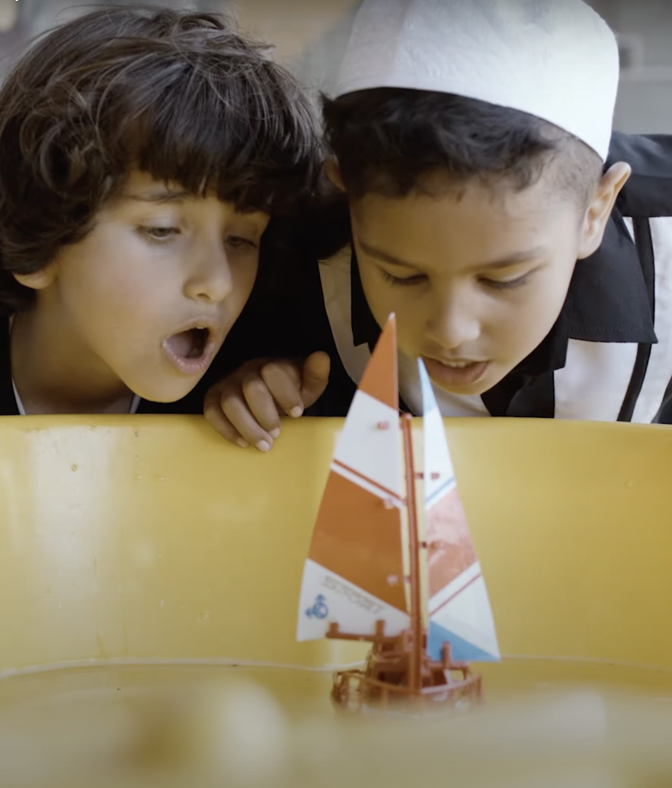 two children blowing on a toy sailboat