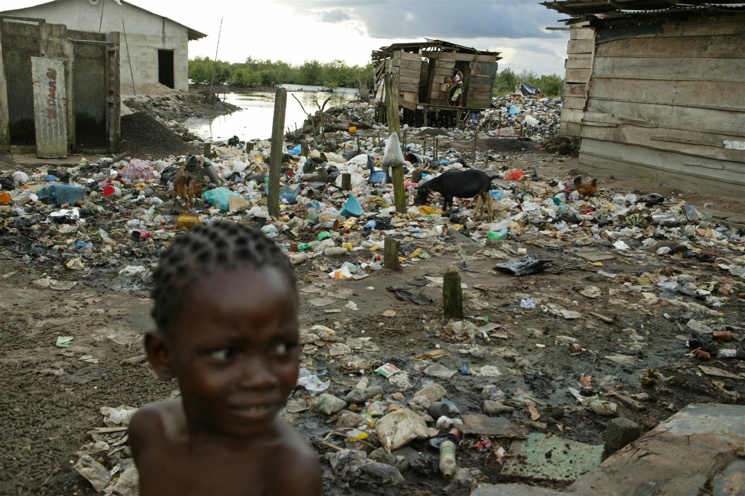 A girl stands amid garbage, mud and human waste in an impoverished village.