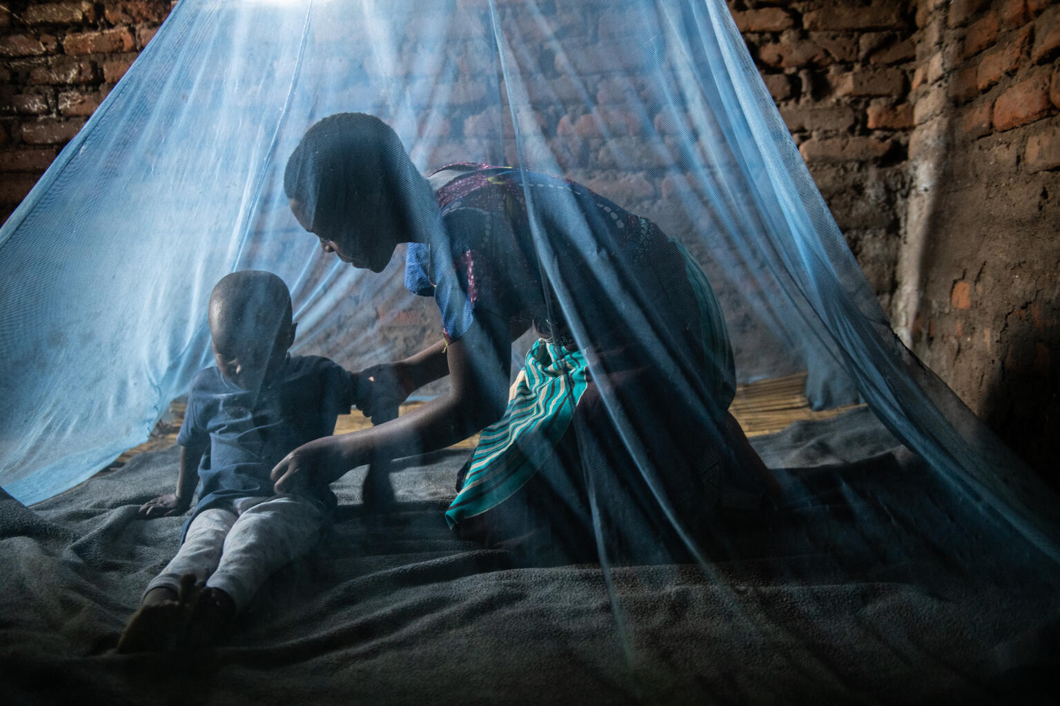 20-year-old Mika John helps her four-year-old son Raymon Mandela to sleep in a mosquito net at their home, Therere Village in Nsanje southern Malawi on Wednesday 15 May 2024.